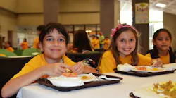 Students in summer clothes eat lunch in a school cafeteria