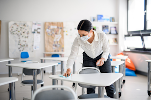 Teacher sanitizing desks at school