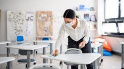 Teacher sanitizing desks at school