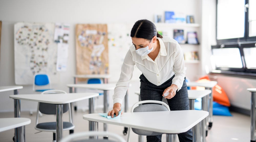 Teacher sanitizing desks at school