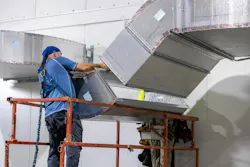 Man installs ductwork system in building wearing safety harness.