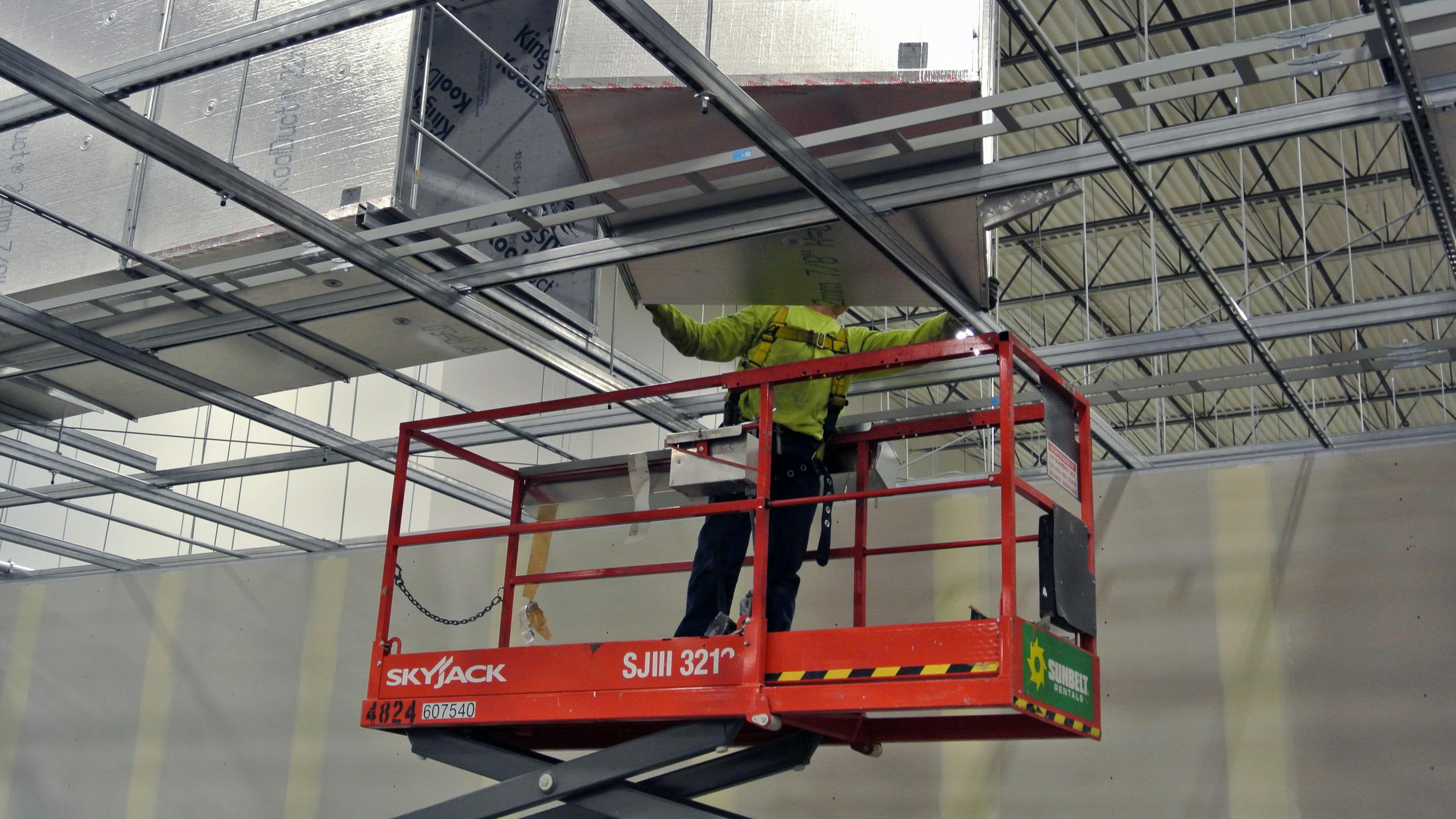 Man on lift installing duct work in industrial facility.