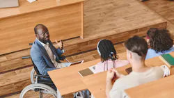 African professor with disability sitting in wheelchair giving lecture to group of students in auditorium