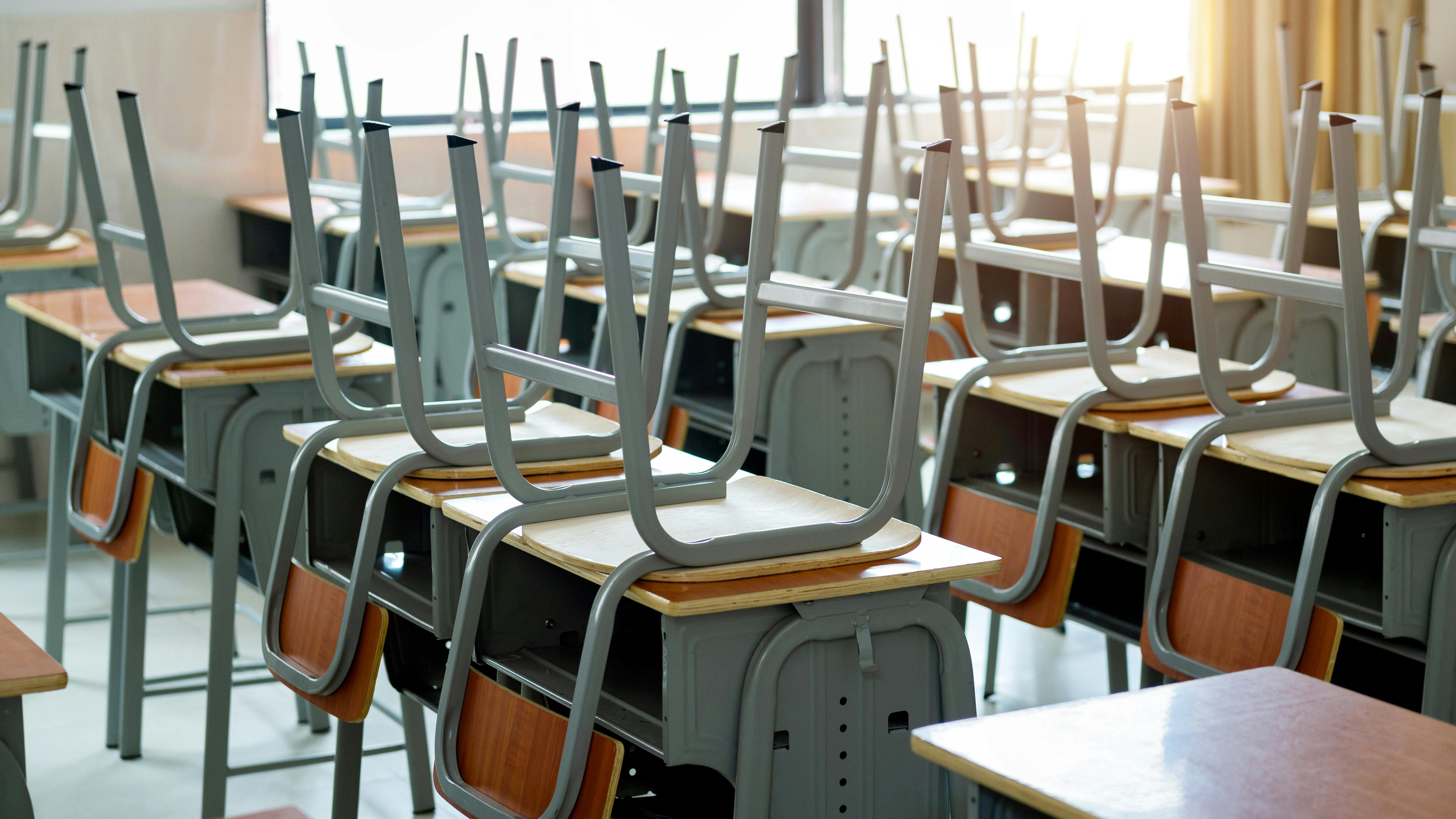 Close-up of chairs left upside down on school desks in empty classroom.
