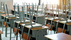 Close-up of chairs left upside down on school desks in empty classroom.