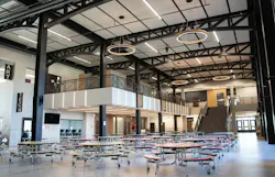 Modern two-story school cafeteria with concrete floors and circular overhead lighting.