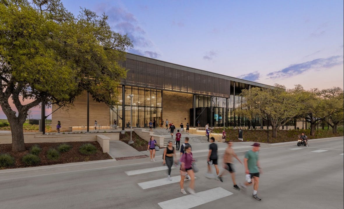 Still-frame image of video about student rec center at Texas A&M showing exterior of building with students crossing street.