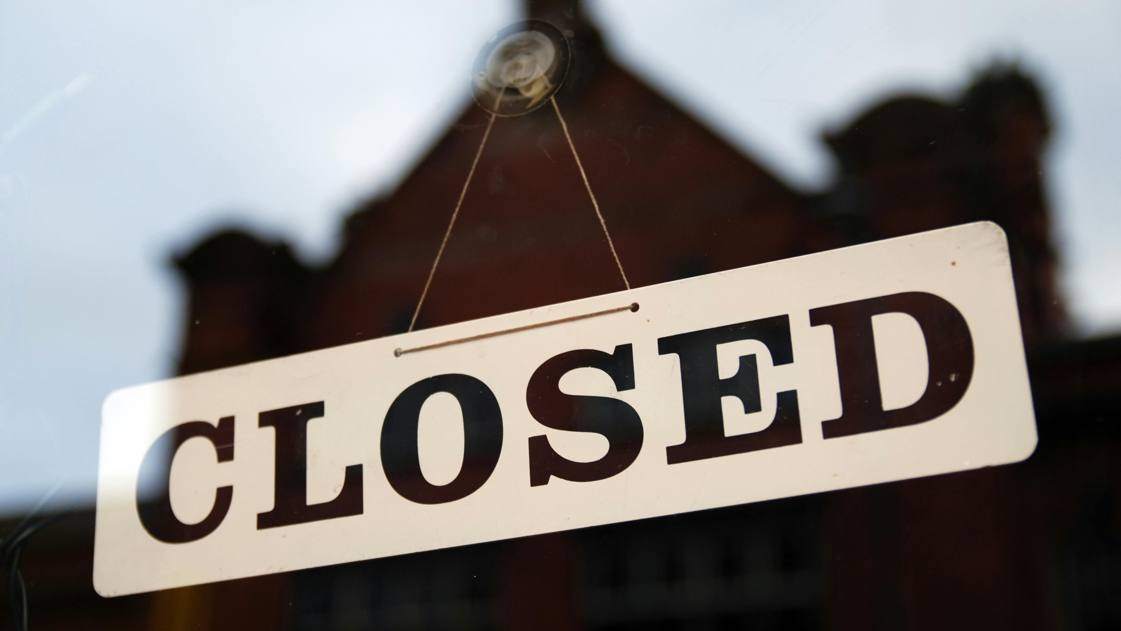 Close-up of closed sign in window with reflection of building blurred in the glass.