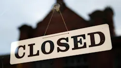 Close-up of closed sign in window with reflection of building blurred in the glass.