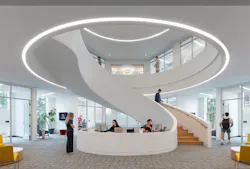 Modern, white, spiral staircase with reception area at base with people throughout.