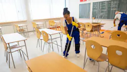 African American woman and Caucasian man wearing uniforms and rubber gloves clean empty classroom with mops.
