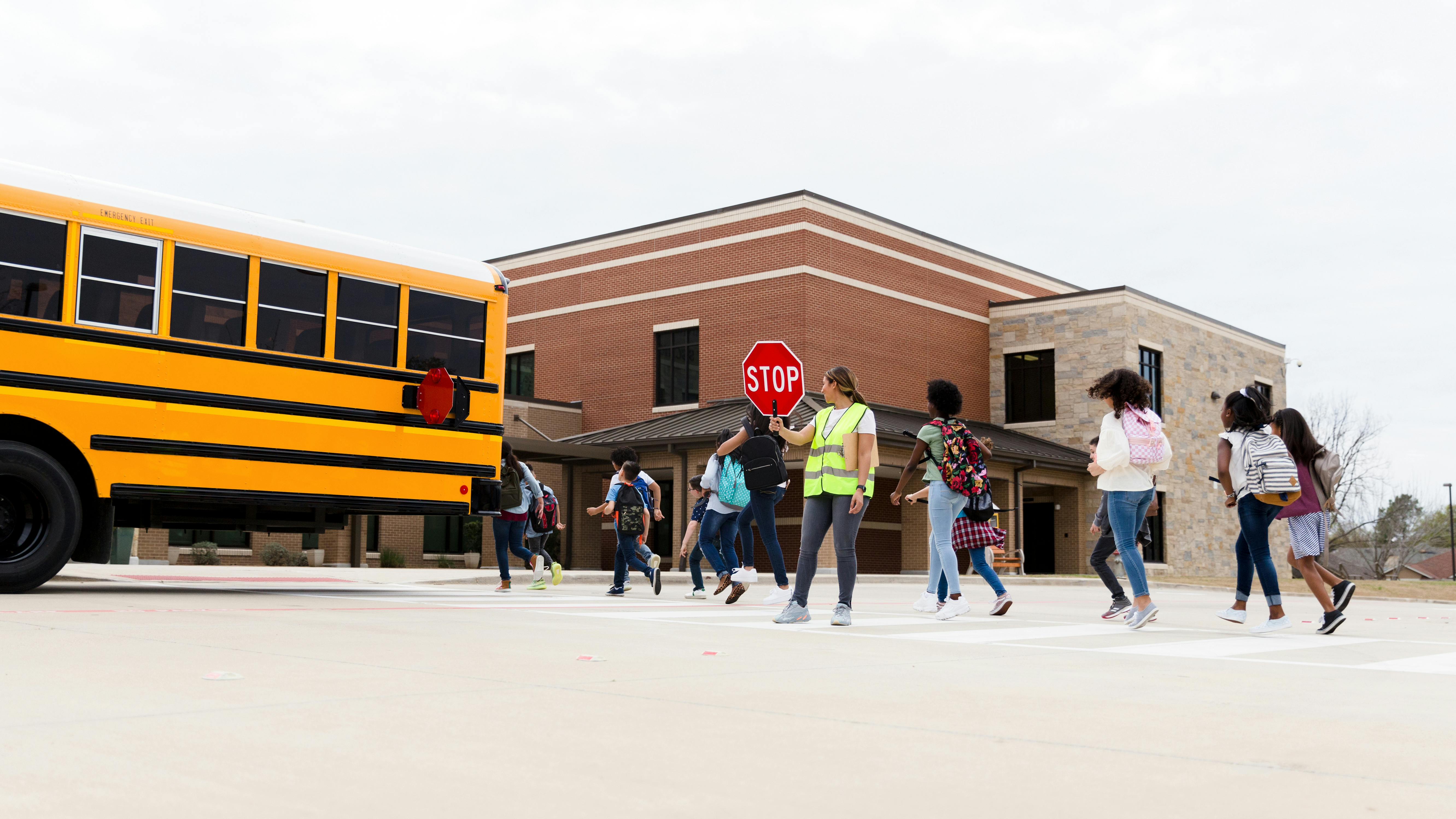 Children get off school bus with crossing guard on duty.