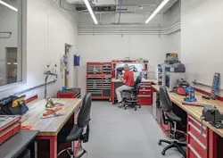 Fabrication room with desks and work benches and man sitting in chair at back of room.