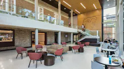 Two-story renovated dining hall with seating at bottom of staircase featuring brick and wood detailing on walls.