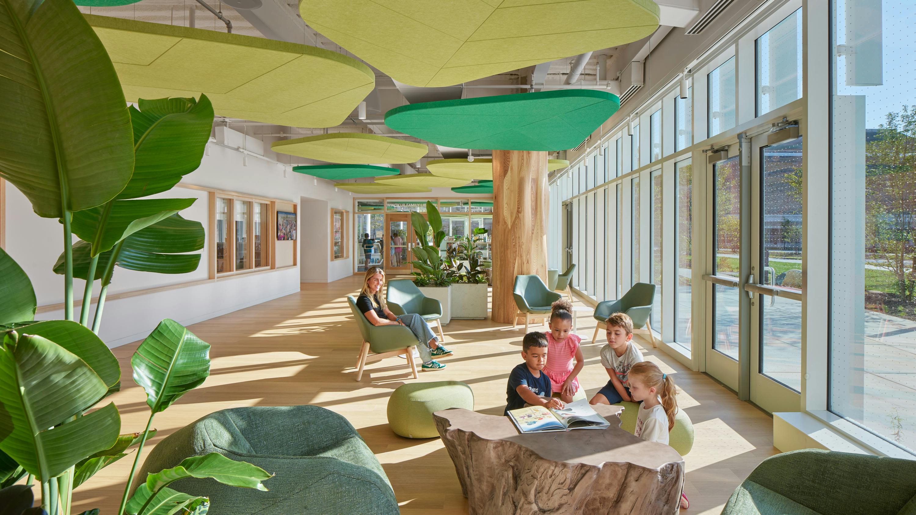 Daylit seating area with students reading among plants and biophilic acoustic ceiling panels in the shape of plants.
