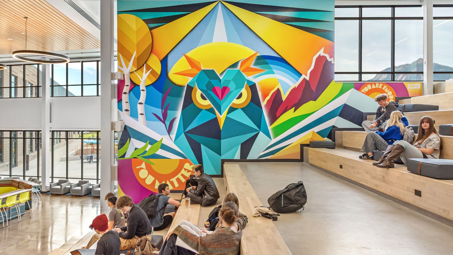 Students sit on reading stair next to large, colorful wall mural of an owl by a local Colorado artist.