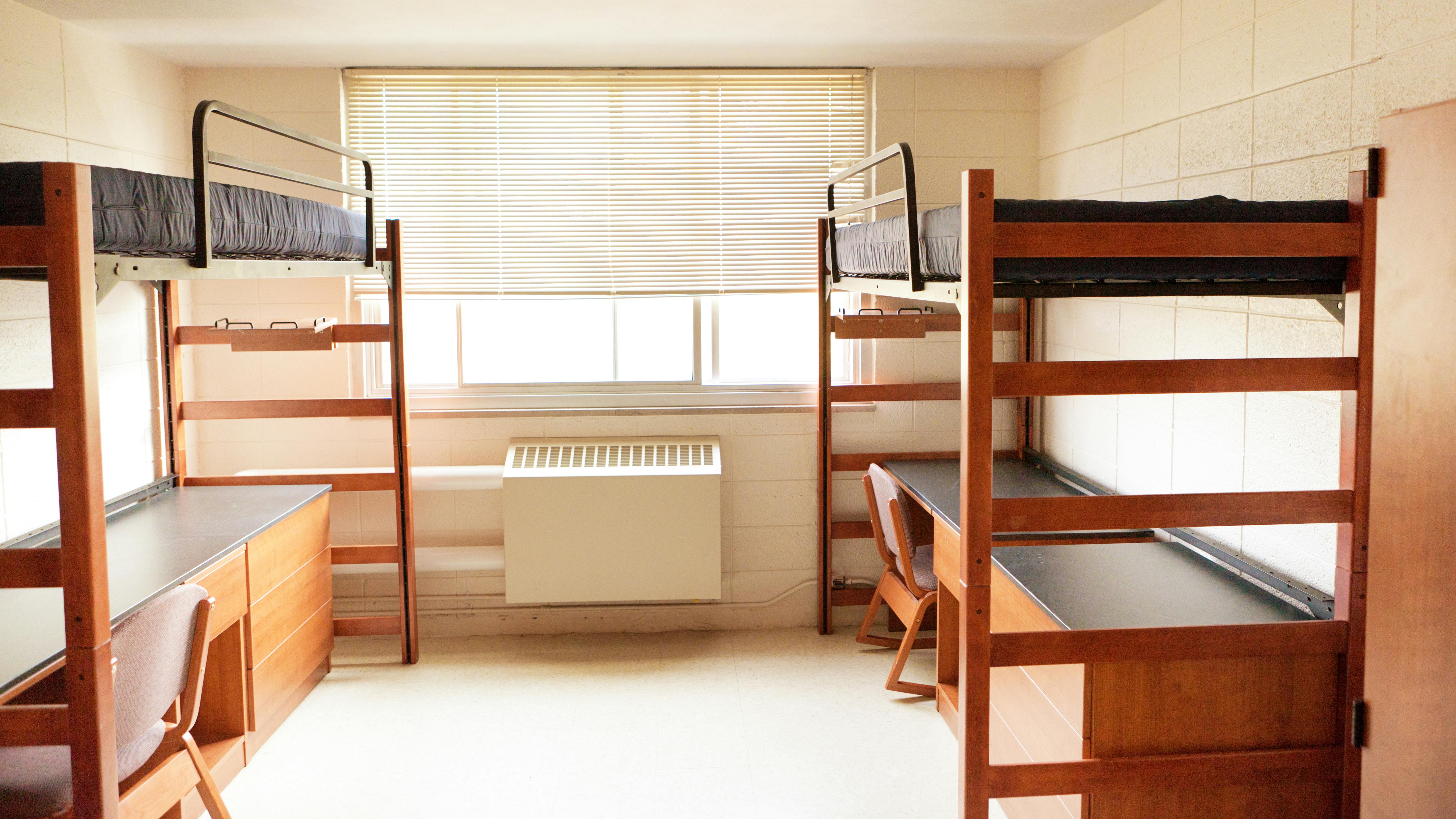 Vacant college dorm room with bunk beds and desks below.