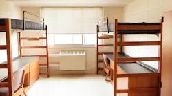 Vacant college dorm room with bunk beds and desks below.