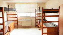 Vacant college dorm room with bunk beds and desks below.