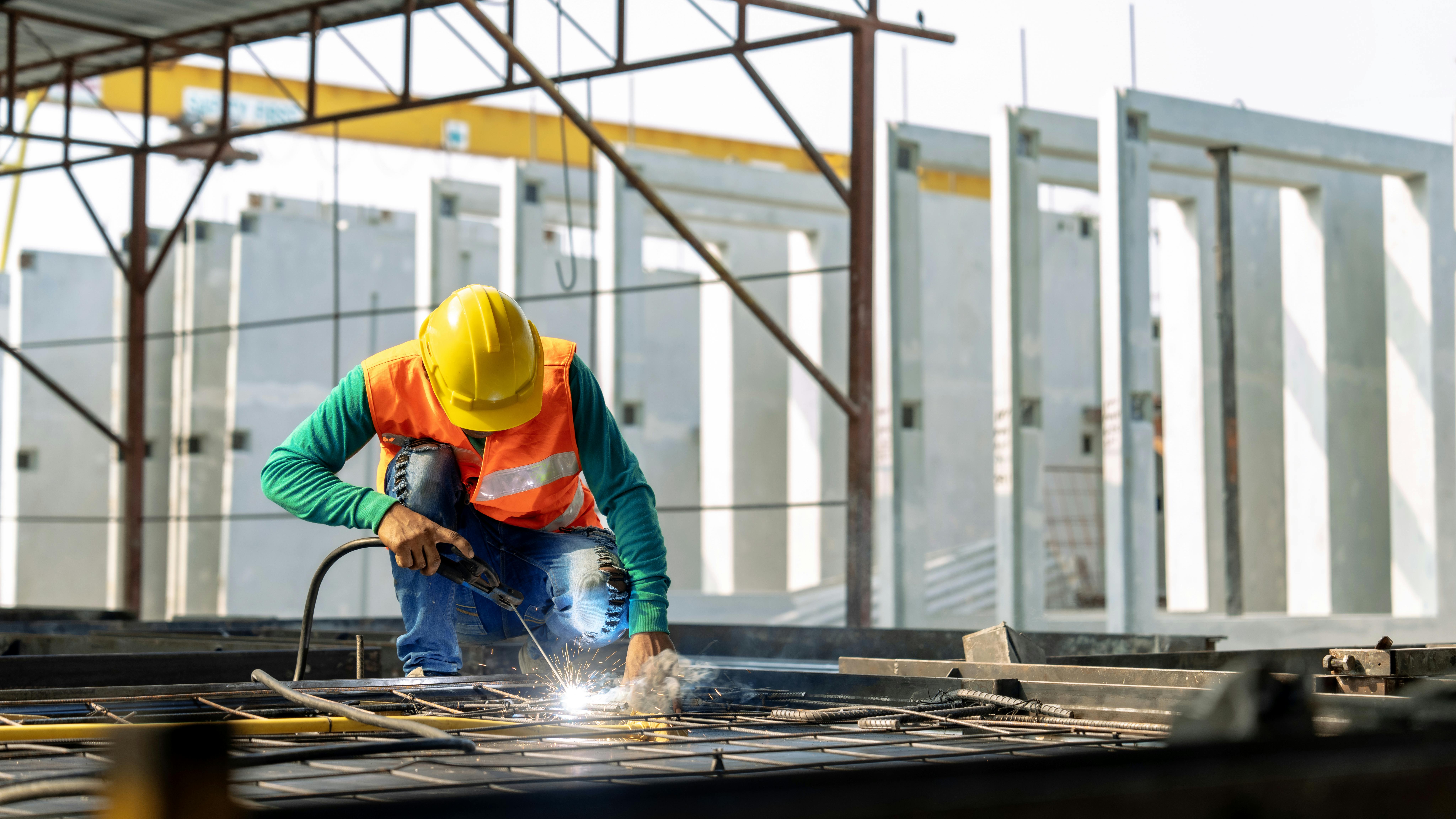 Construction worker wearing safety hat spot welding rebar on job site.