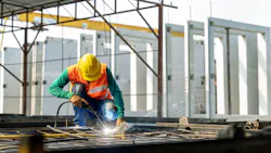Construction worker wearing safety hat spot welding rebar on job site.