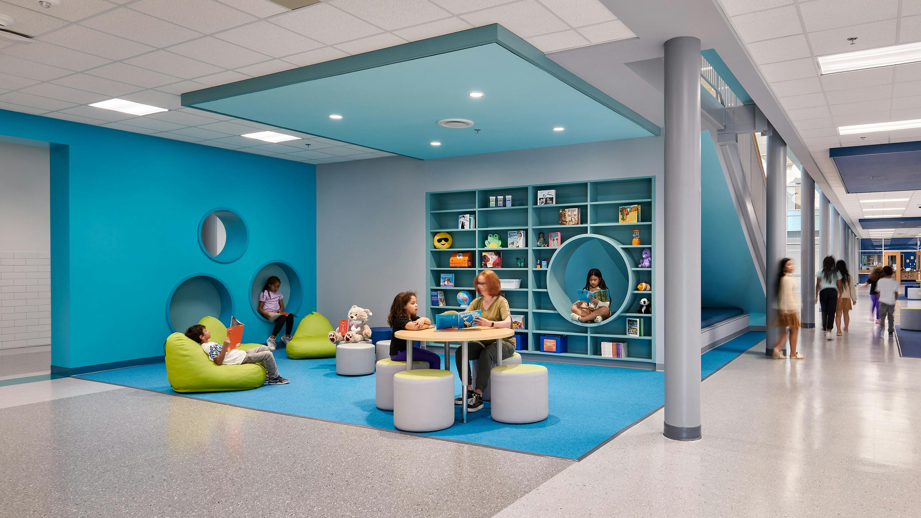 Teacher sitting with student in colorful, casual learning area with table, soft seating and cubbies in the background.