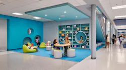 Teacher sitting with student in colorful, casual learning area with table, soft seating and cubbies in the background.