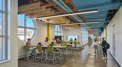 Students gather in a casual study space next to circular windows with wood ceiling baffles hanging above.