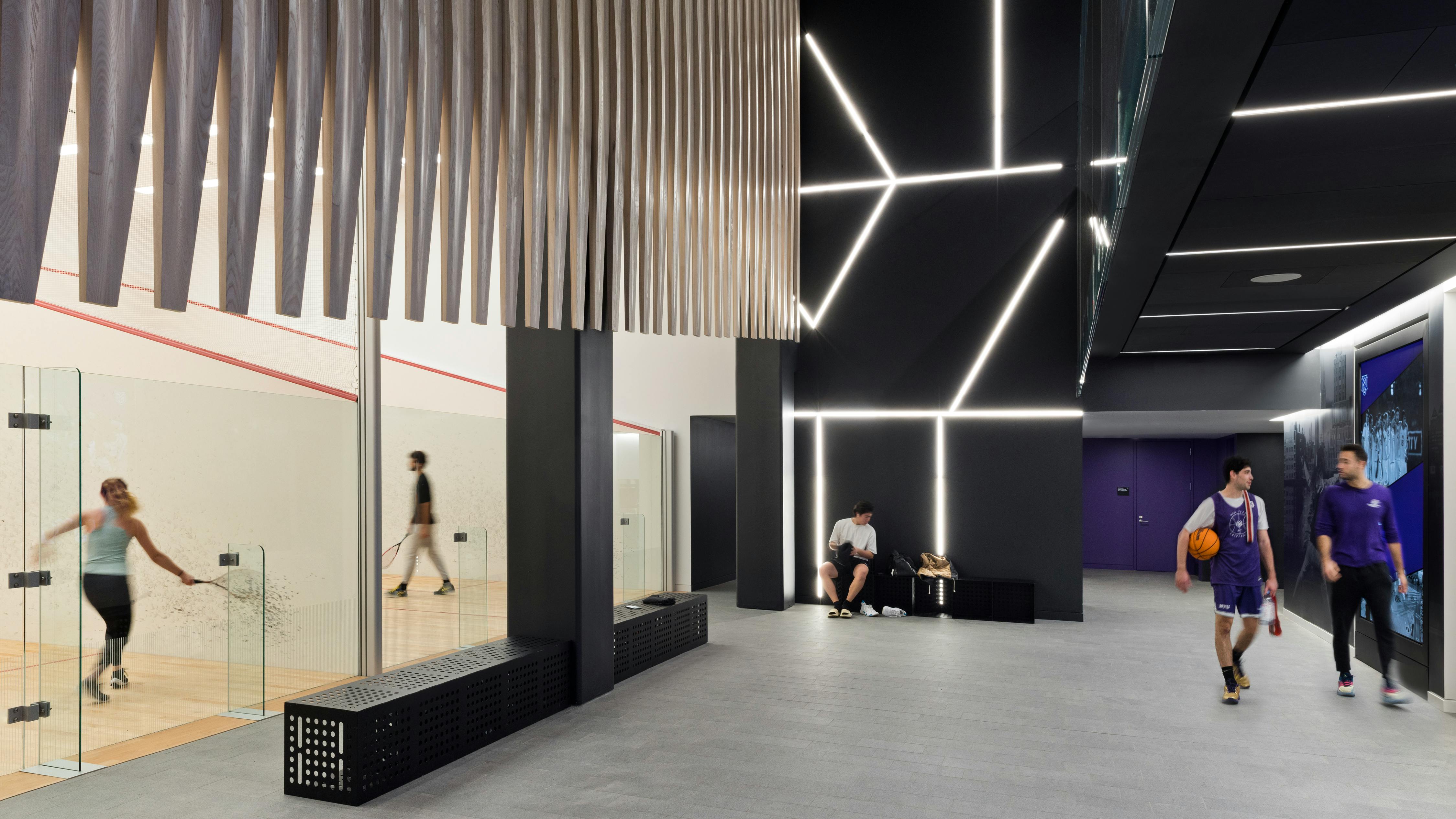 Modern college athletic center with indoor racquetball courts and students walking in hallway with basketball.