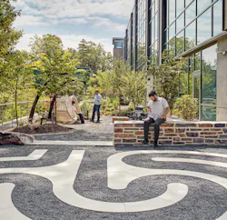 Students sit in outdoor courtyard space with greenery and gravel walkway.