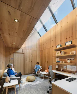 Student and mental health counselor sit in wood-paneled office with clerestory windows and desk in foreground.