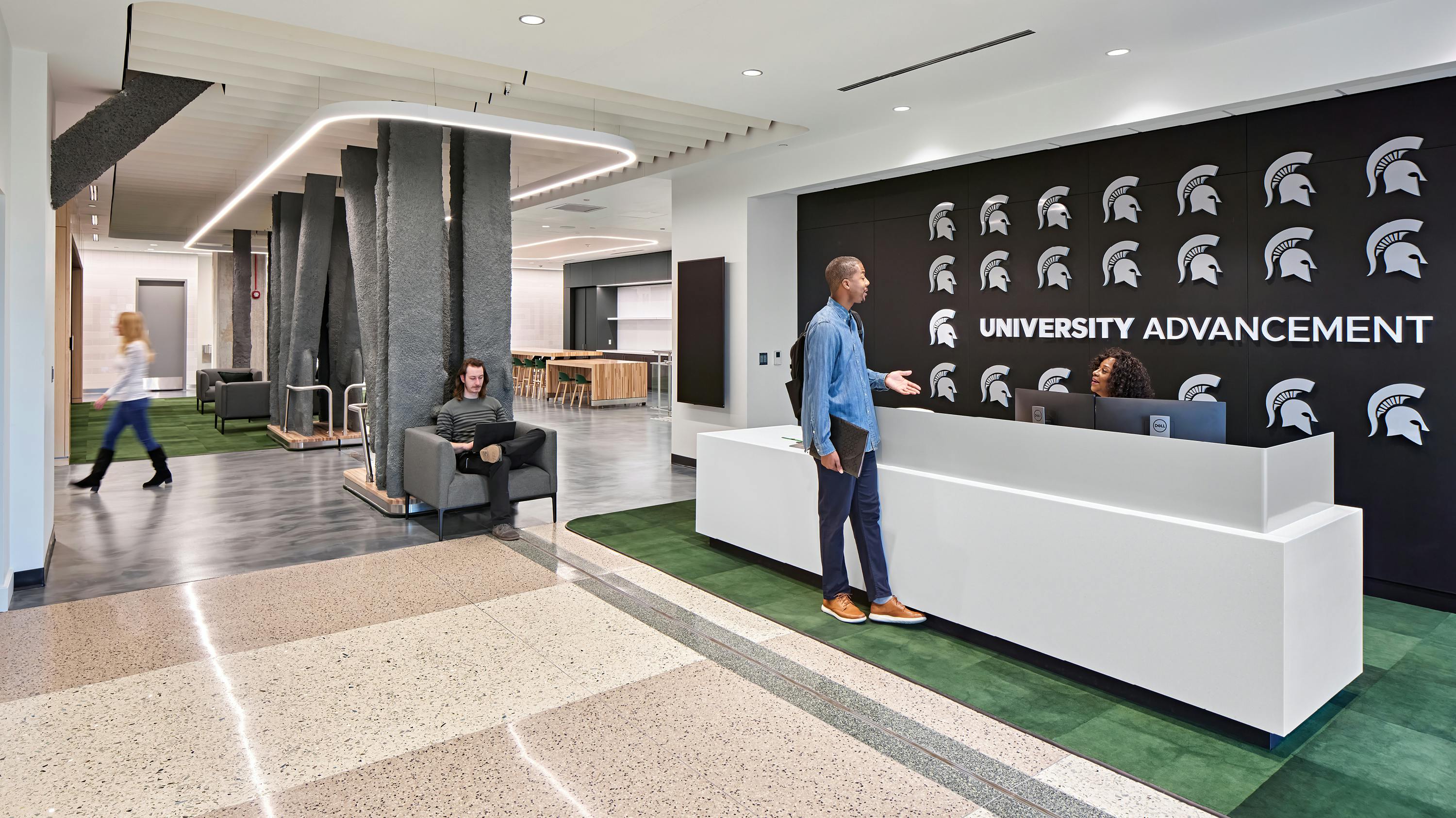 Reception area with student talking to receptionist against black wall with university logo.