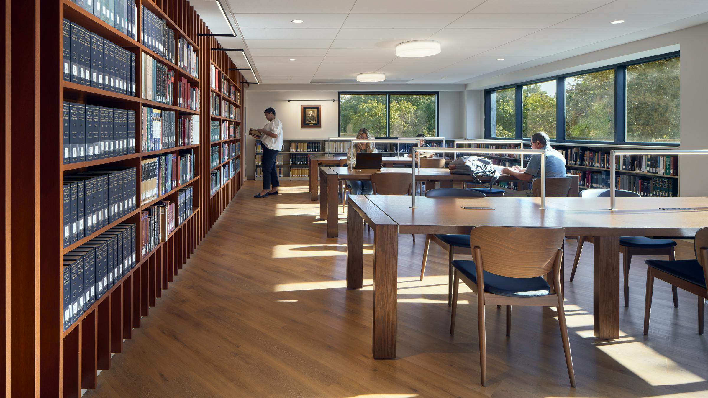 Seminary library with bookshelves on the left and tables with chairs for study with students.