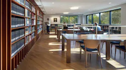 Seminary library with bookshelves on the left and tables with chairs for study with students.