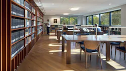 Seminary library with bookshelves on the left and tables with chairs for study with students.