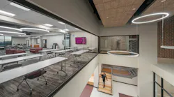 Two-story atrium with glass wall showing desks and chairs in classroom with modern, circular lighting above.