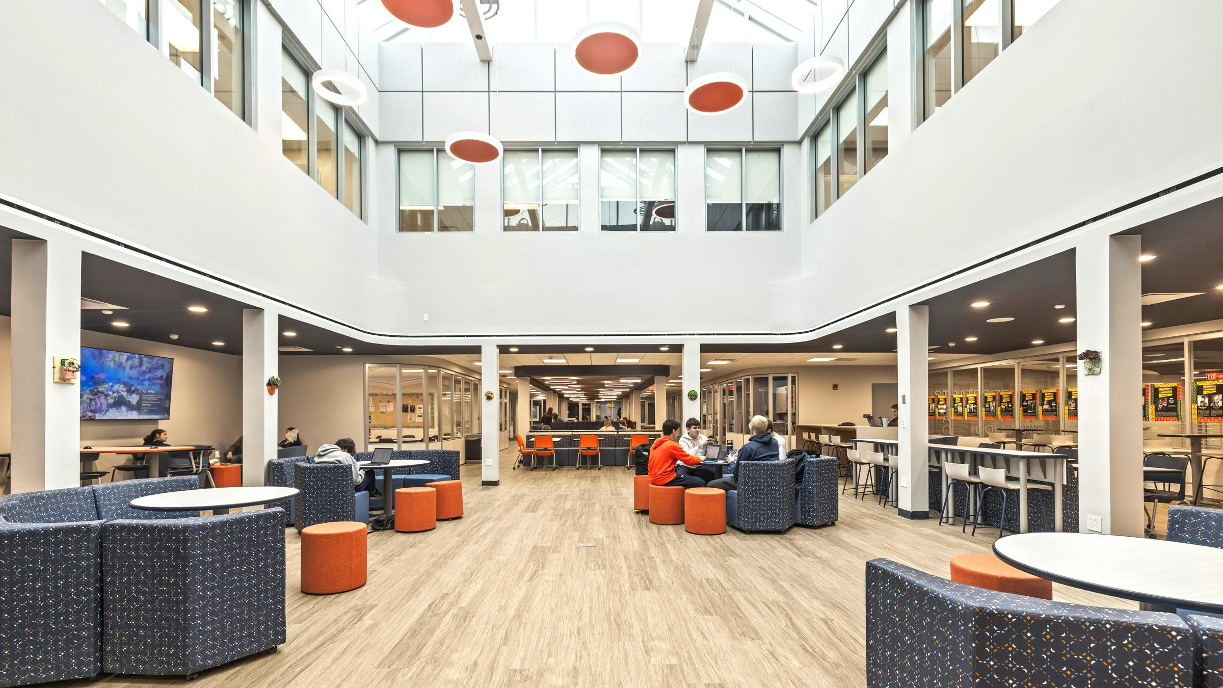 Bright, two-story daylight atrium with skylights and a variety of colorful lounge seating occupied by students.