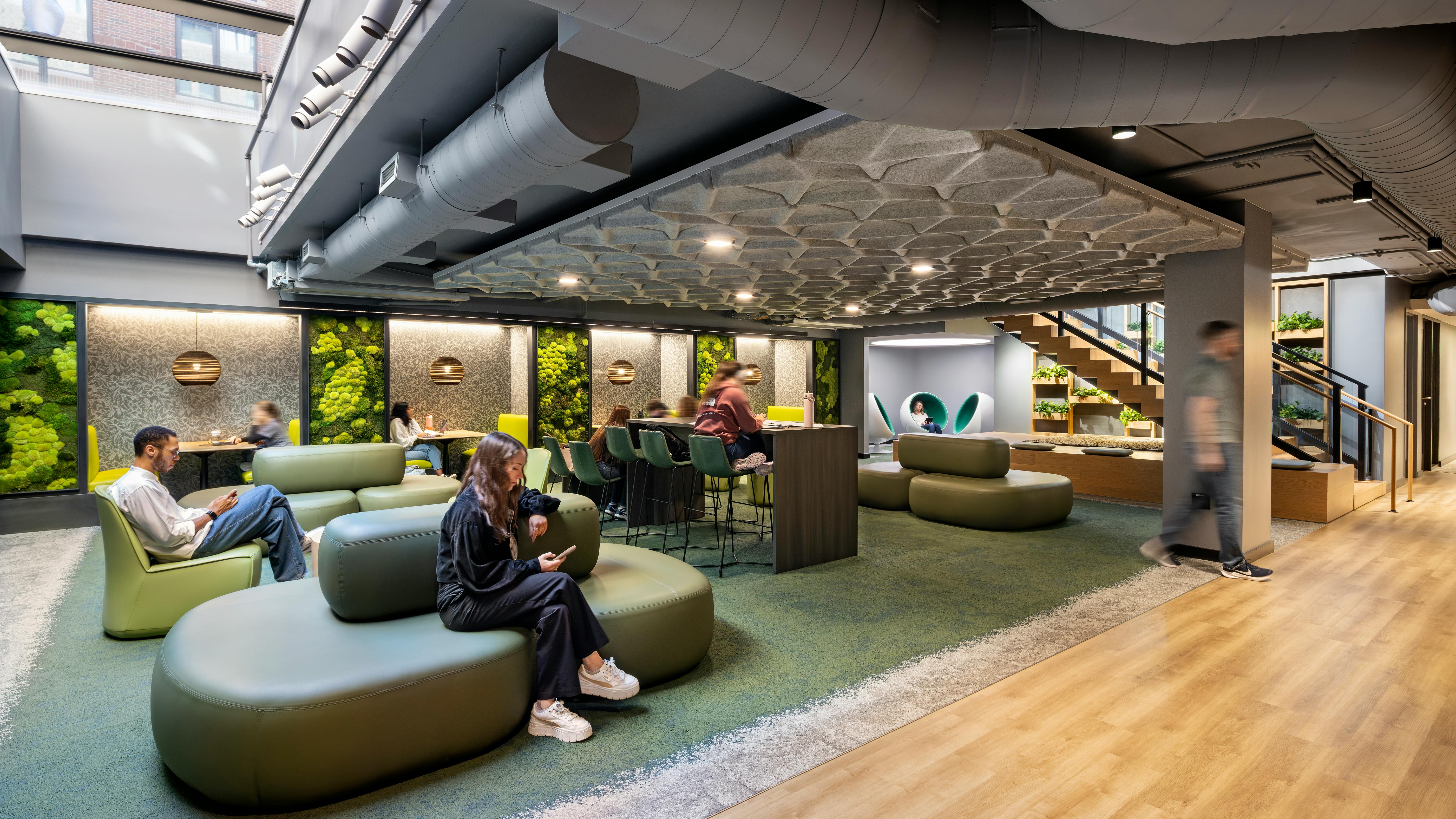 Students sit in lounge area with comfortable seating and living plant walls beneath skylight.