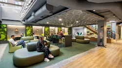 Students sit in lounge area with comfortable seating and living plant walls beneath skylight.