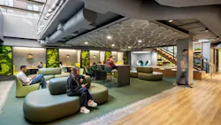 Students sit in lounge area with comfortable seating and living plant walls beneath skylight.