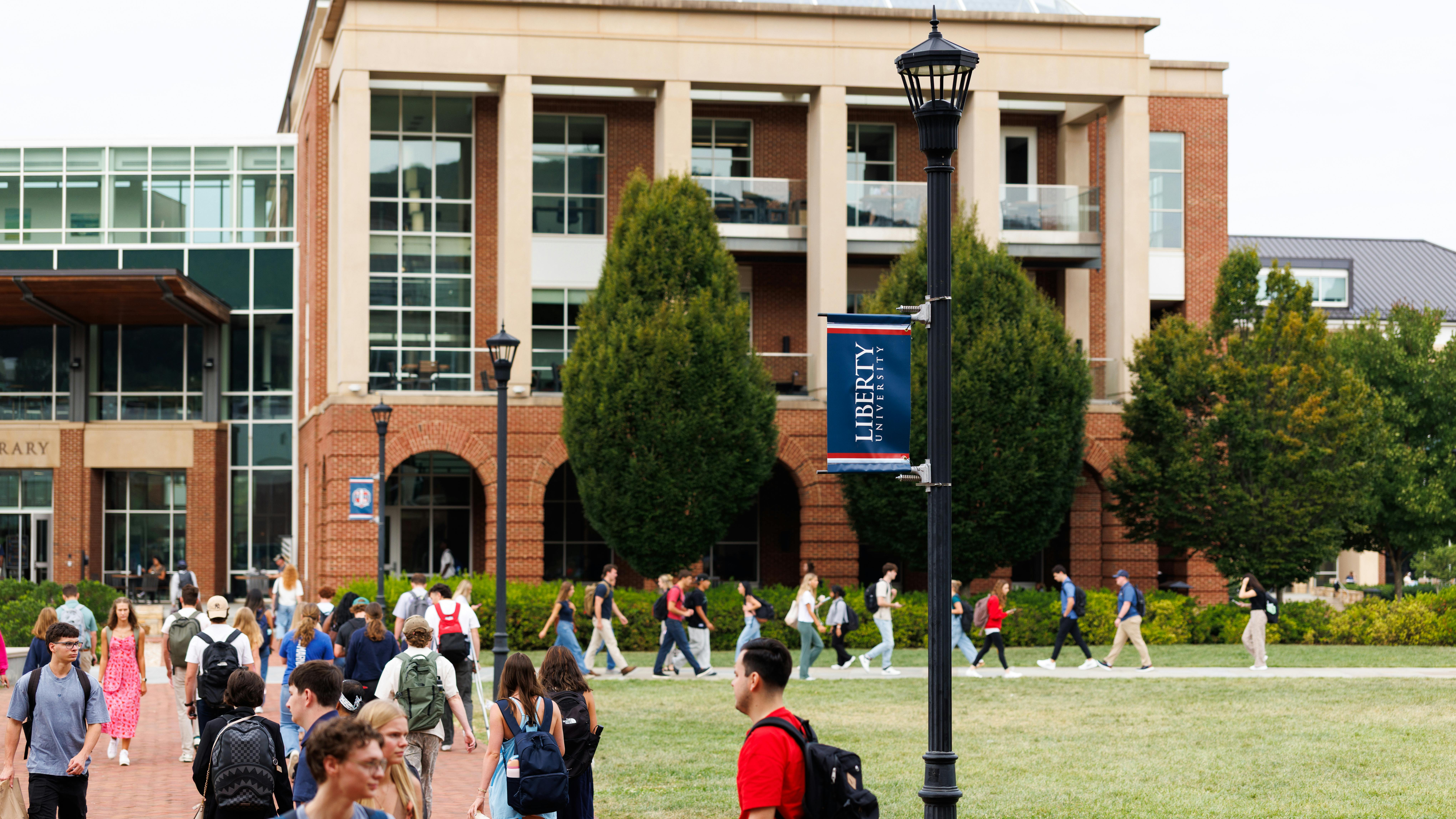 Students walk across campus lawn in front of academic building at Liberty University.