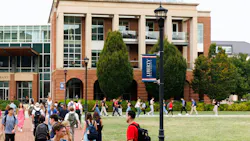 Students walk across campus lawn in front of academic building at Liberty University.