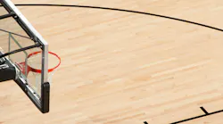 Above a side view of a basketball hoop with clear back board above a wooden court.