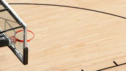 Above a side view of a basketball hoop with clear back board above a wooden court.