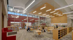 Large, open media center with bookshelves and students sitting at desks under circular and linear lighting fixtures.