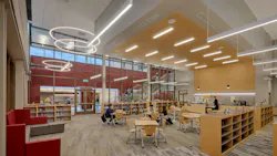 Large, open media center with bookshelves and students sitting at desks under circular and linear lighting fixtures.