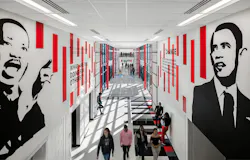 Second-floor view of daylit hallway in high school where students are walking with murals of MLK, Jr. and President Barak Obama above on walls.
