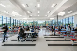 Busy and bright high school cafeteria full of students with floor-to-ceiling windows in background.