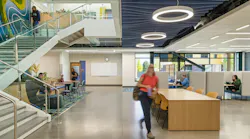 Two-story learning facility with staircase and people sitting at various seating and study areas. Acoustic baffles and circular lighting fixtures at ceiling.