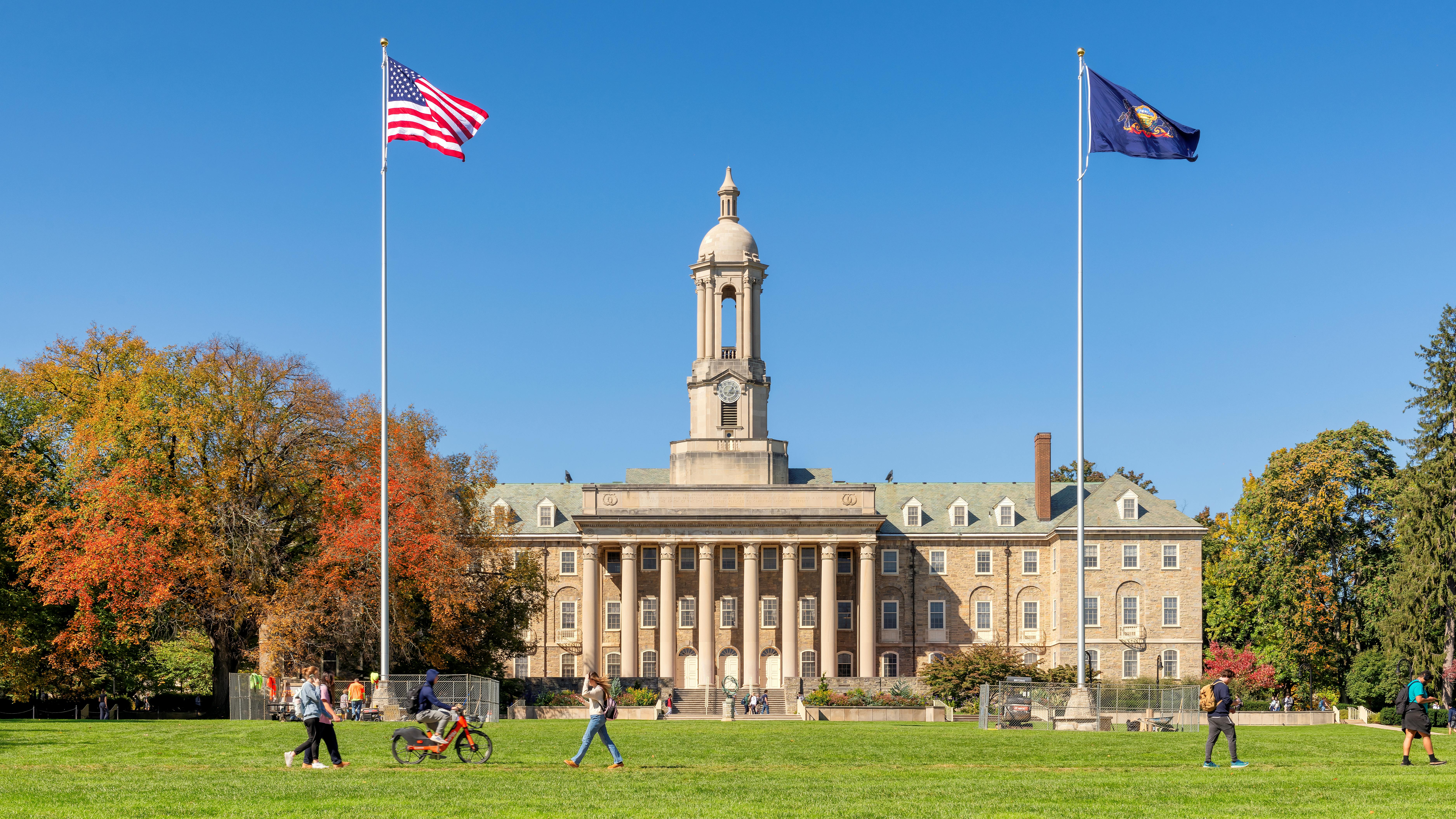 The Old Main building on the campus of Penn State University in autumn sunny day with students walking and biking.